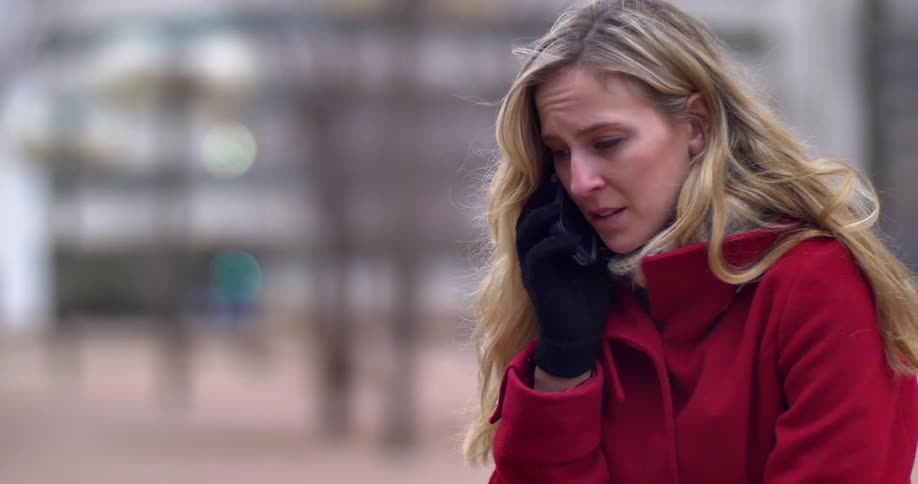 A woman looking very sad as she talks on her cell phone outside