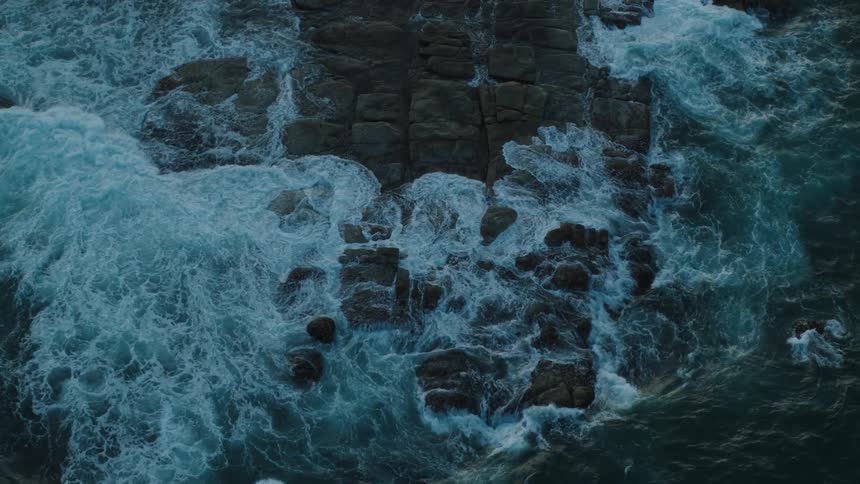 Drone view of waves crashing against and over rocks on the coast