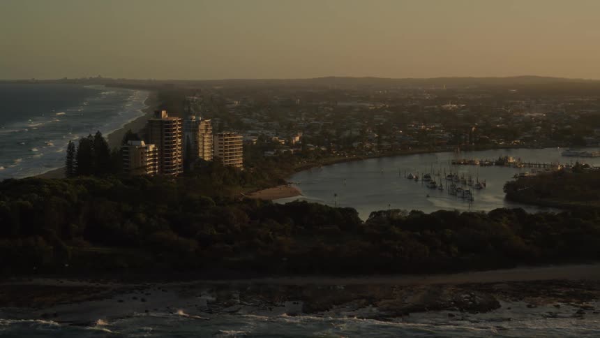 A lush peninsula with tower buildings and trees with a side to a waterway leading to the ocean