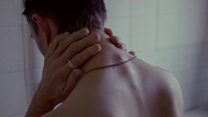 The backside of a man in the shower with his hands behind his neck looking down at the floor thinking