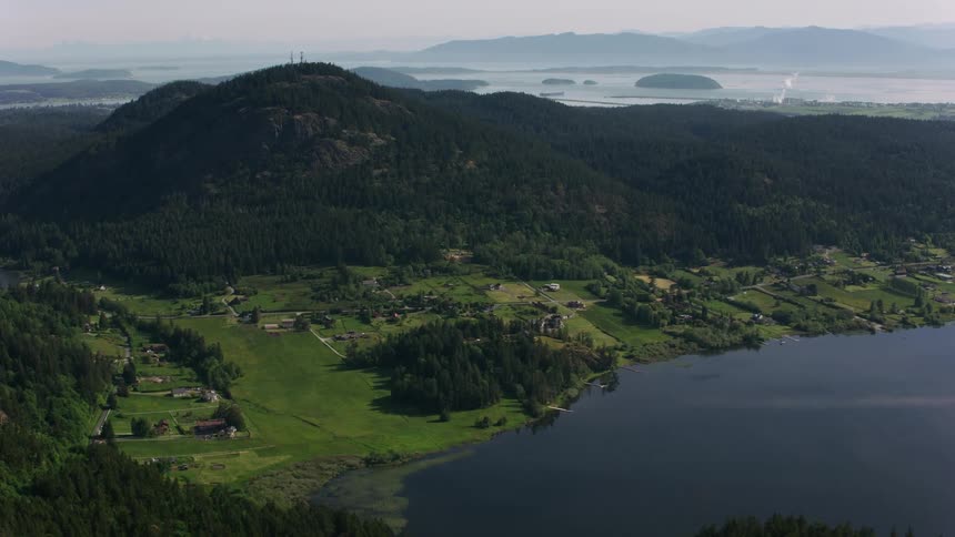 Aerial view of mountain valley with lake and forest greenery ocean in the background late day