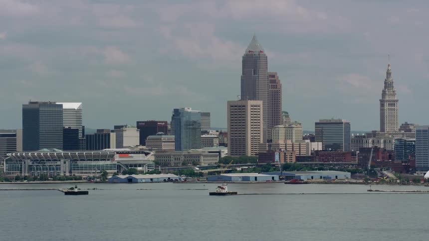 Boats sail in the lake as traffic moves on the highway outside a city along the coast with tall buildings and skyscrapers on the skyline
