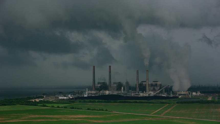 Smoke rises from the smoke stacks of a factory along the coast under a dark stormy sky