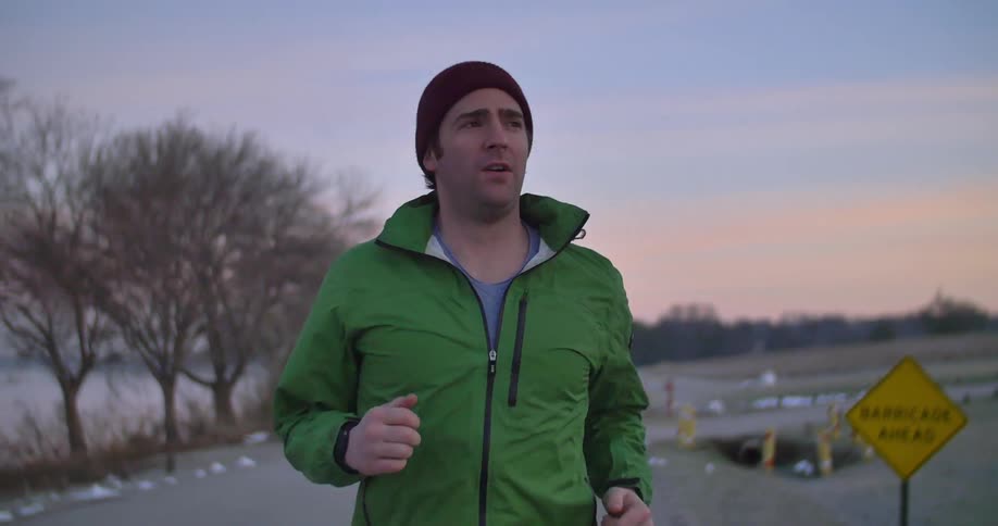 A man slowly jogging along a coastal road during sunrise