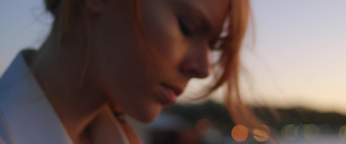 Woman with red hair and a white shirt sits and writes things down in a notebook outdoors at dusk