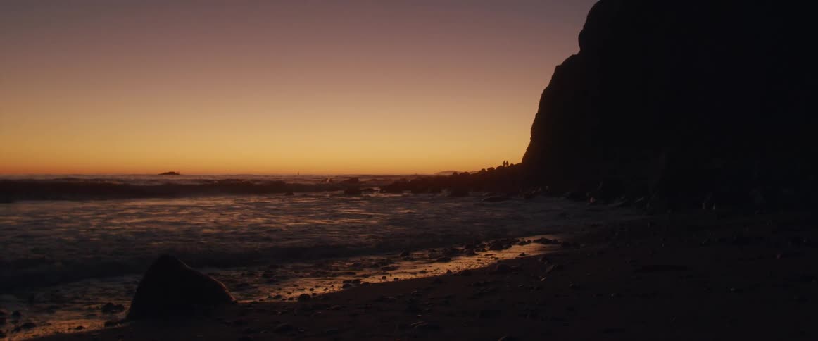 Silhouette of a mountain on the shores of a beach next to the ocean at sunset
