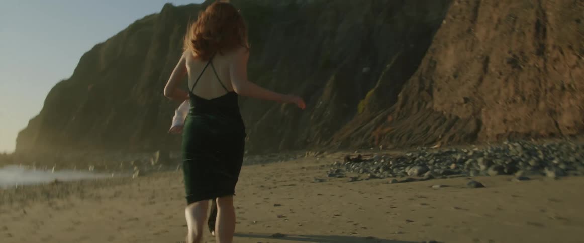 Man with a shirt pants and a woman with a black dress run across beach at dusk