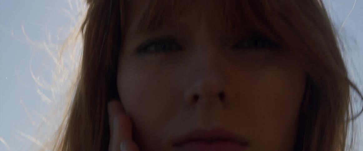 Woman with red hair touches her cheek and looks at the camera under the shining sun
