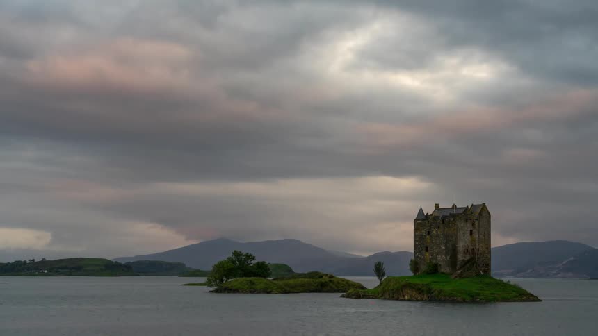 A castle on an island in the middle of a body water on a cloudy day