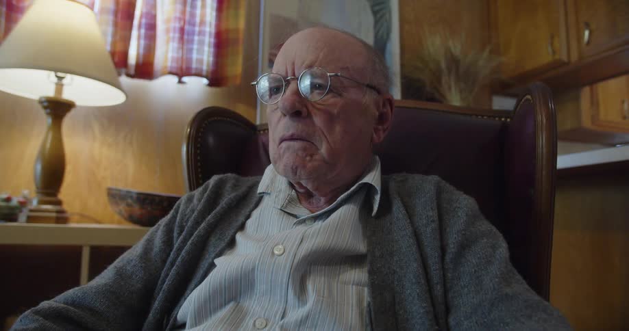 Elderly man stops to stare and think in middle of reading a newspaper