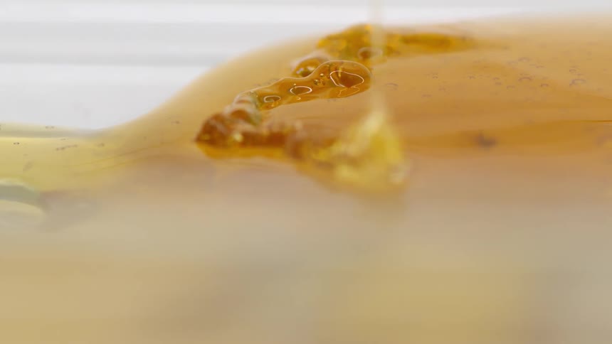 Amber syrup drizzles across surface of existing mass of syrup