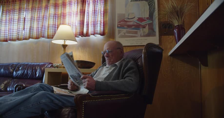 An elderly man is sitting and reading the paper