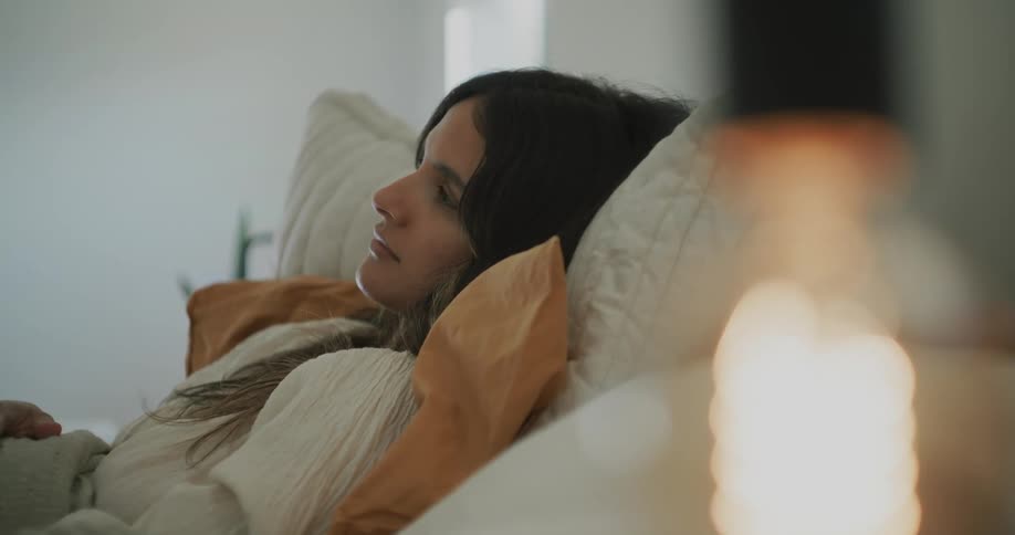 A woman is lying on the couch on a pillow as she turns her head and looks to her side