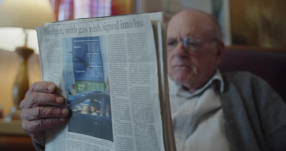 An old man reads a newspaper in a chair