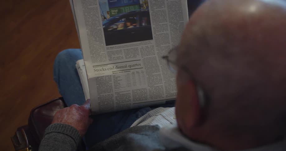 Elderly man sits in chair and reads newspaper