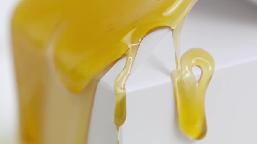 Close up of light clear yellow honey pouring over white corners