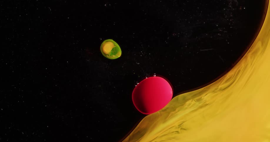 Yellow fluid flows across black dotted with particles before it impacts reddish ball a distance from a yellow green glob