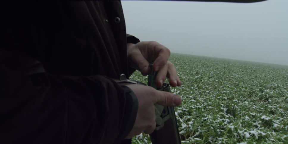 Man loading shells into his shotgun in a field on a cloudy day