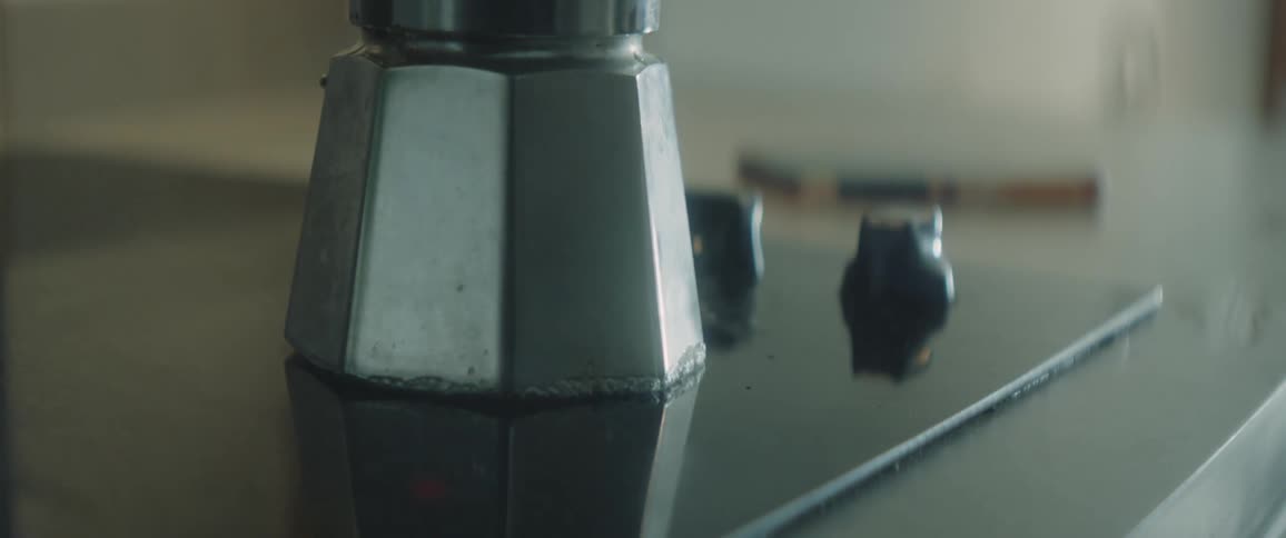 Person casts shadow onto stove top as stovetop coffee maker simmers