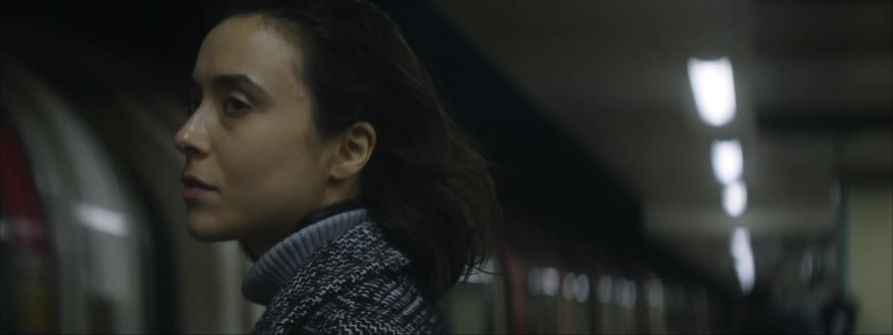 Woman standing in a subway station as her hair blows in the wind as the subway pulls into the station