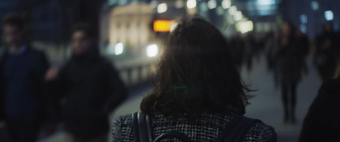 A woman is walking on a busy street and many people are walking past her as she walks into the flow of the crowd