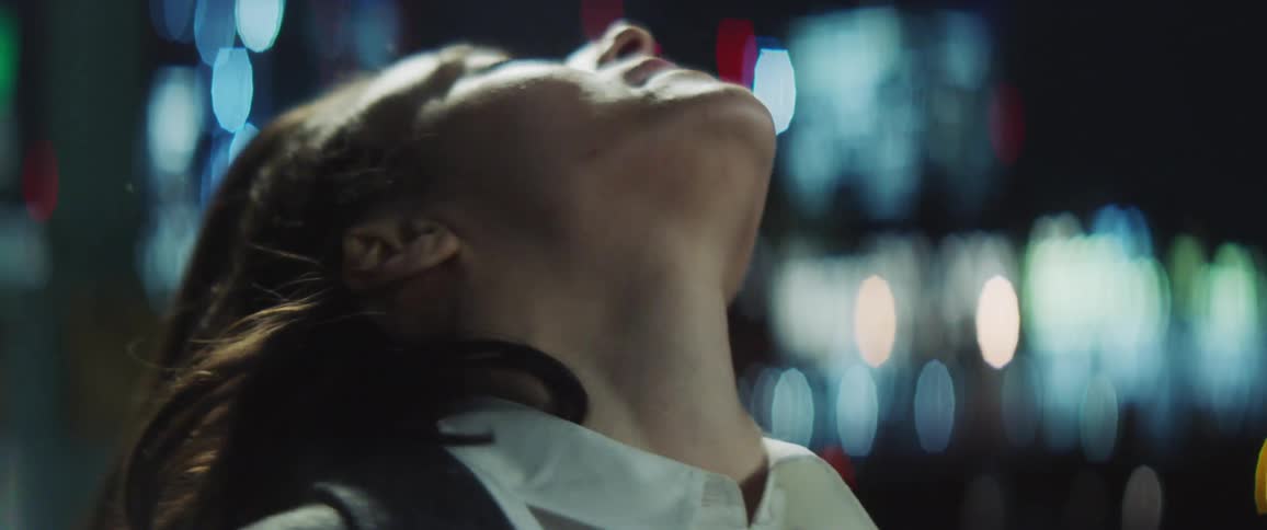 Woman rolls her head on her neck as she stretches against city lights at night