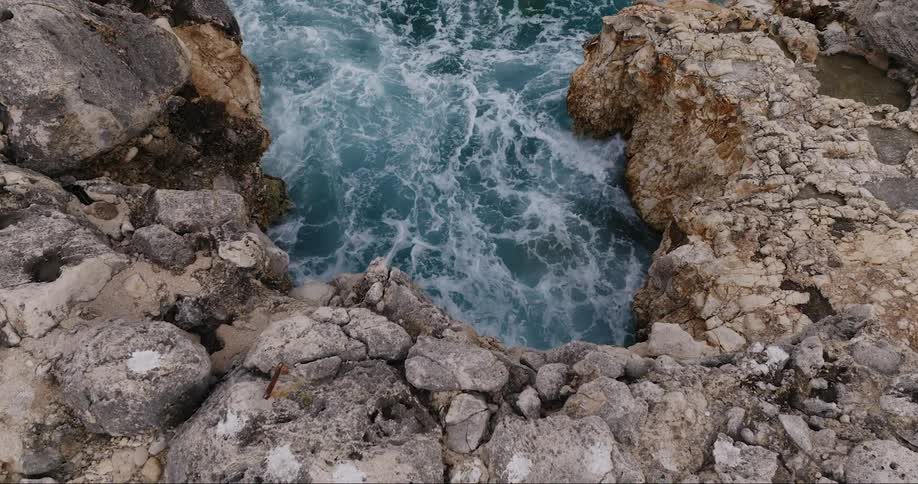 Waves churn at base of slightly raised rocky shore near tidal pools