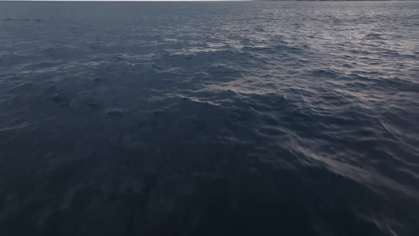 An aerial of the ocean surface with waves crashing and waking over the top