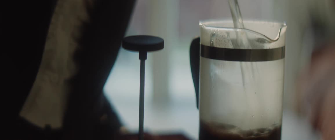 A person pouring hot water out of a kettle into a glass cup creating coffee