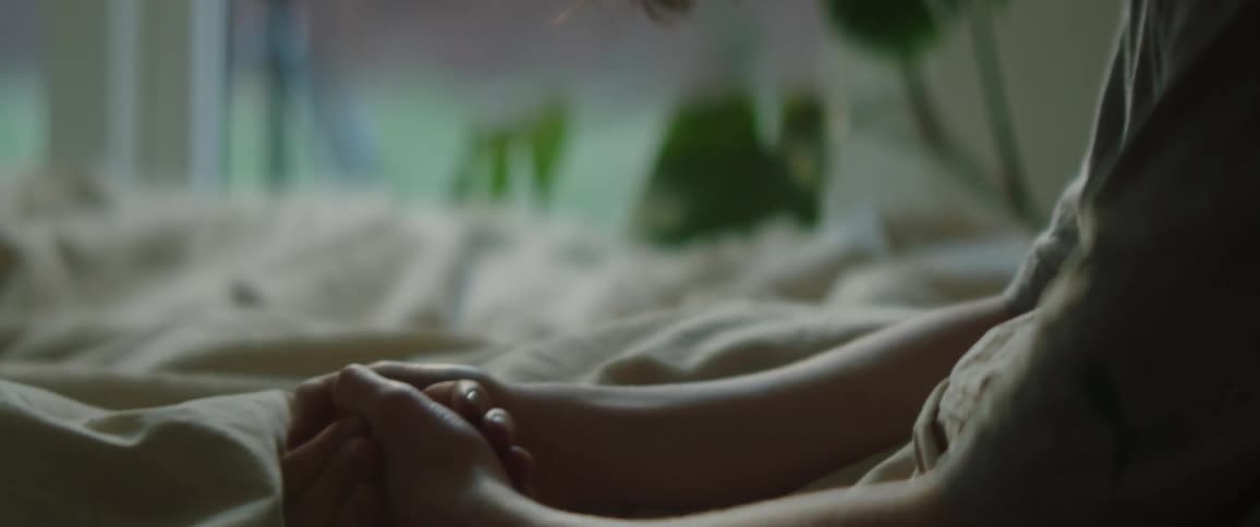 A woman is sitting on her bed near a window
