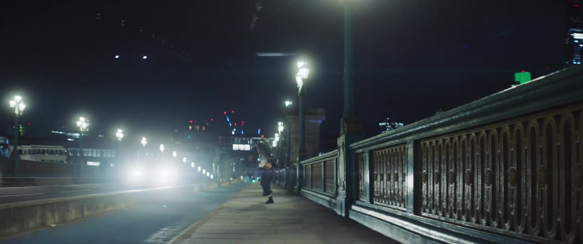 Woman dances along sidewalk on bridge in city at night