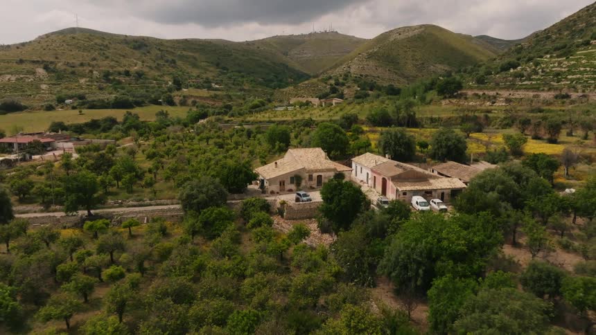 Orchard and crop fields separate houses in valley surrounded by green hills