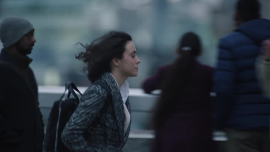 A young woman walking hurriedly through a busy city street while looking around