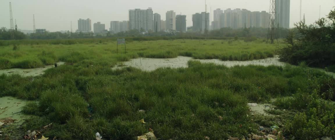 A landfill separated from a large city by a grass field with a pond