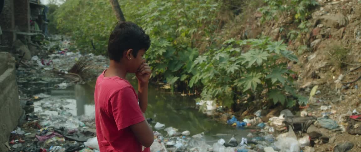 A boy cries while staring at a river filled with garbage