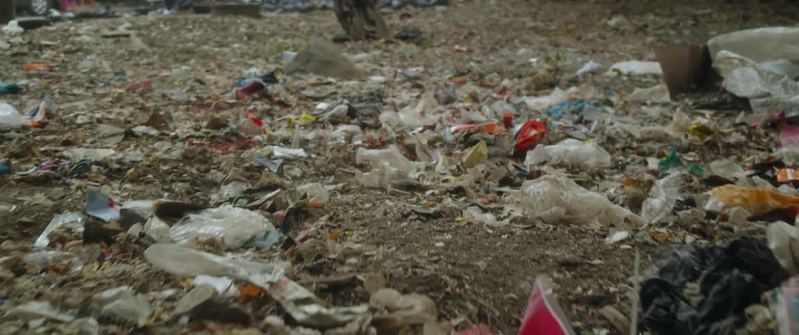 Close up of trash lying on the ground next to a street with parked cars and a person walking
