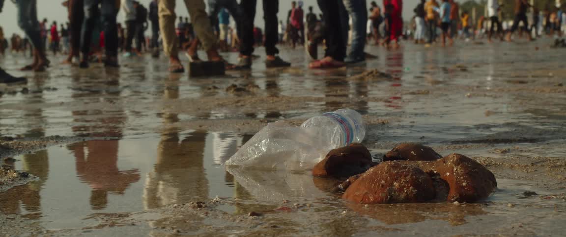 Garbage on sand as crowds of people walk around and stand on the beach