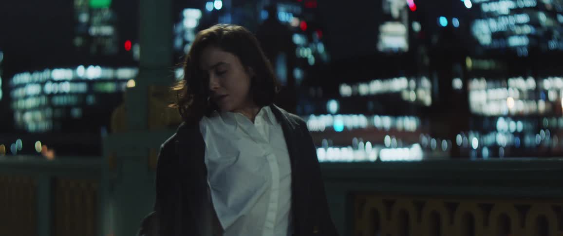 A woman is standing near a downtown street at night as she begins to move her head and arms and dance