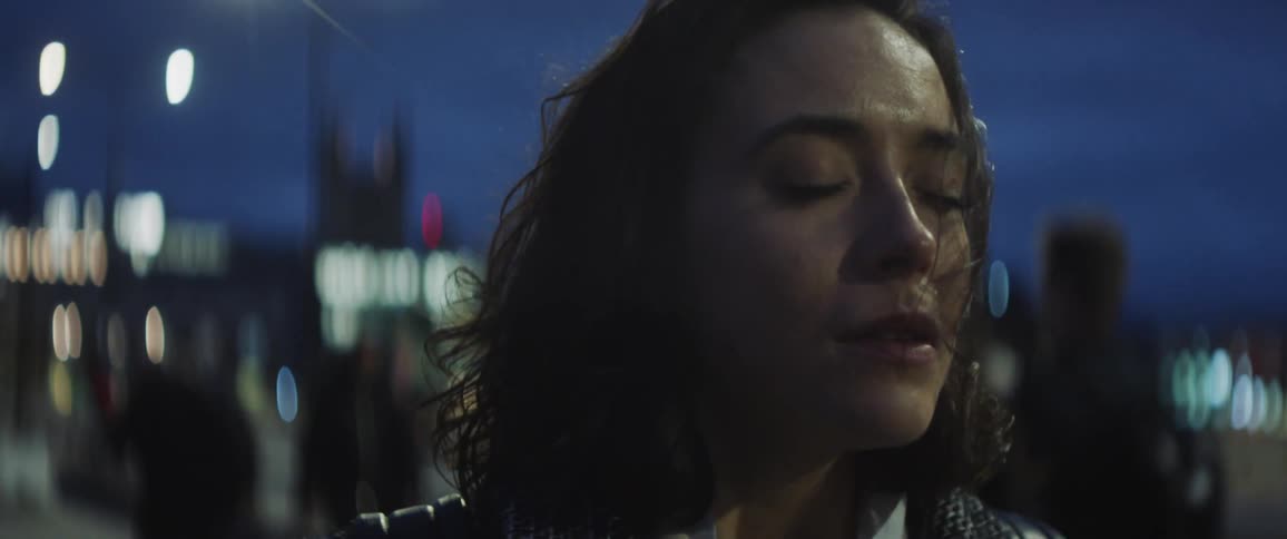 Female pedestrian stops on busy sidewalk at night and stands with her eyes closed