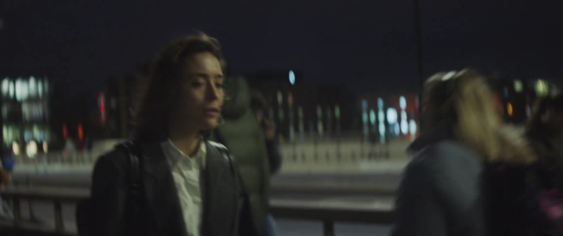 Young woman is walking down crowded city street at nighttime stops to look at something not happy
