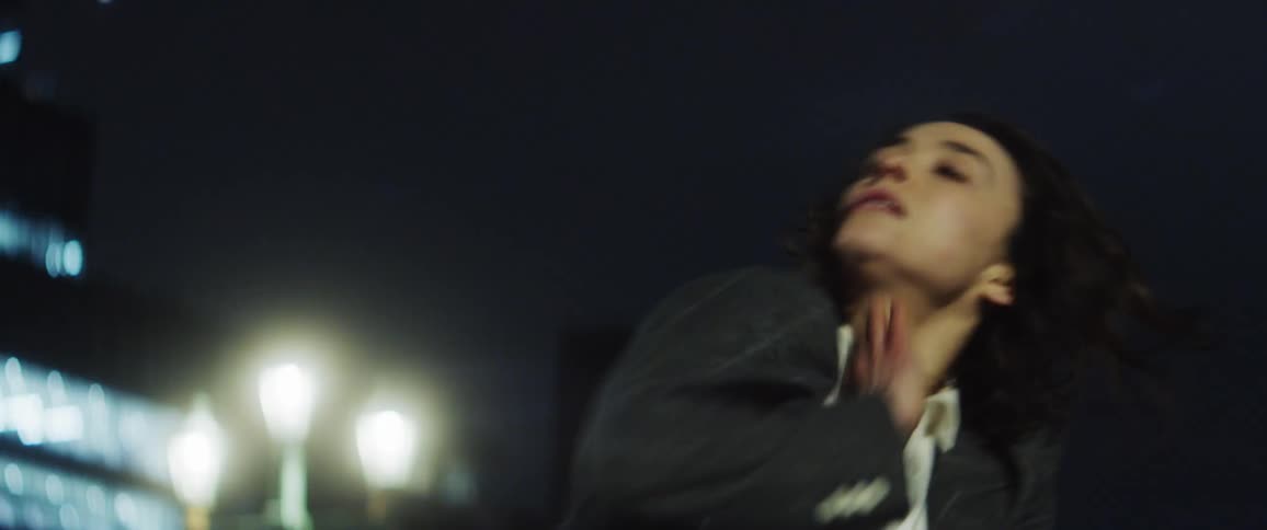 Woman dancing outdoors at night near a tall building lit up
