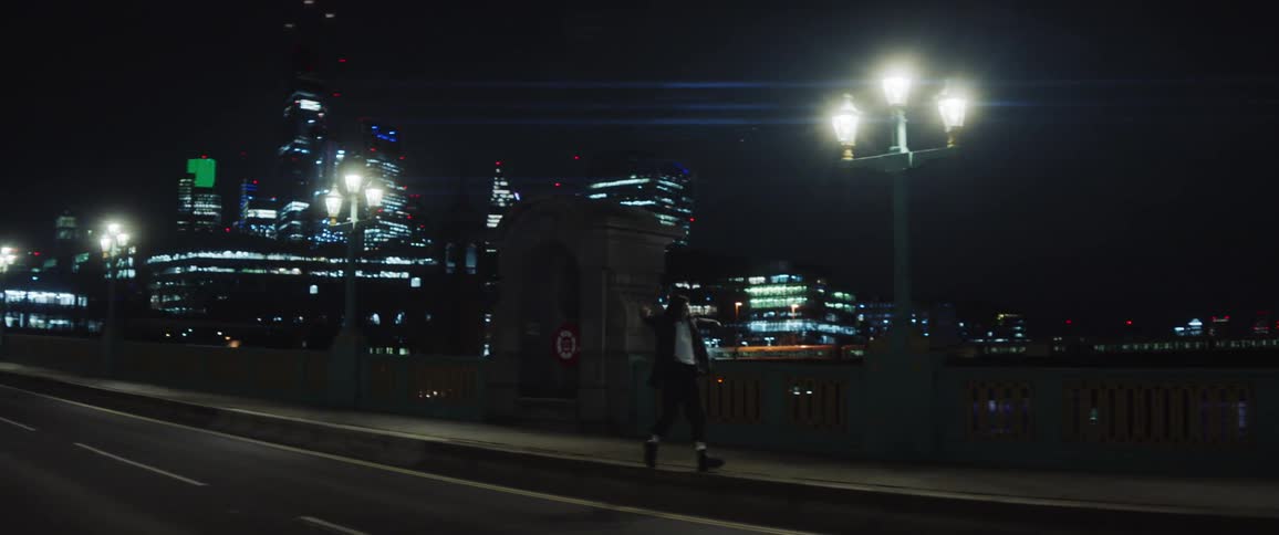 Woman with gray jacket and white shirt and black pants dances on the bridge at night