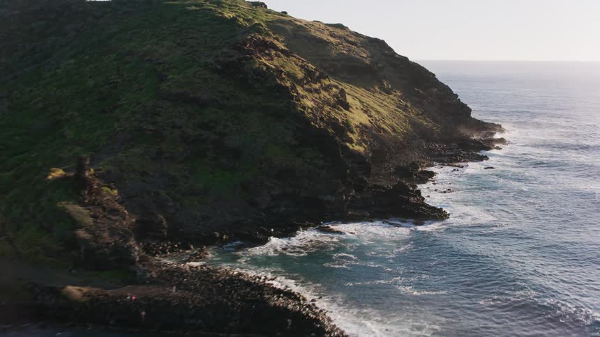 An aerial of a mountain peninsula on the coast as waves crash against the land
