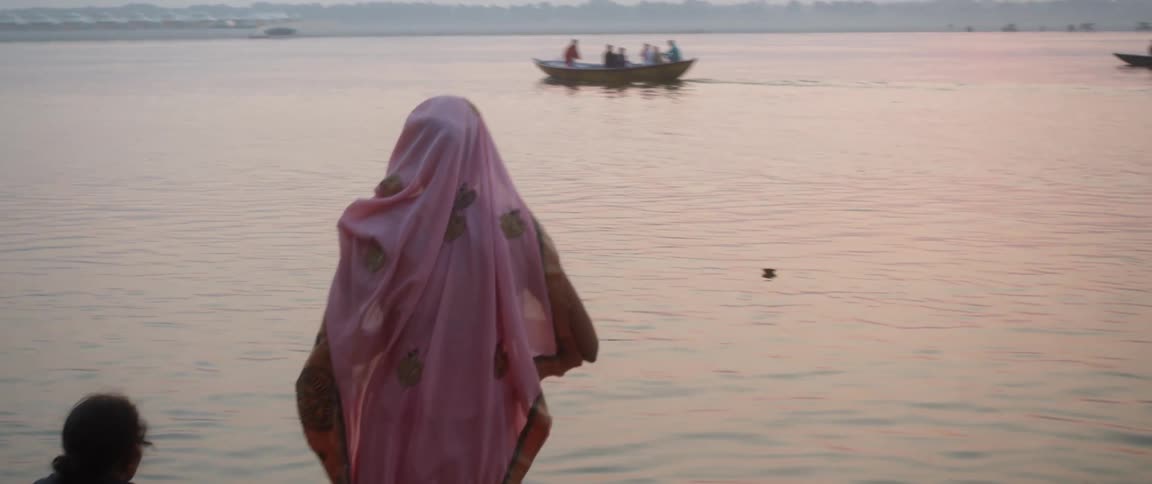 A woman pours water from a jar into a river in a ritualistic manner