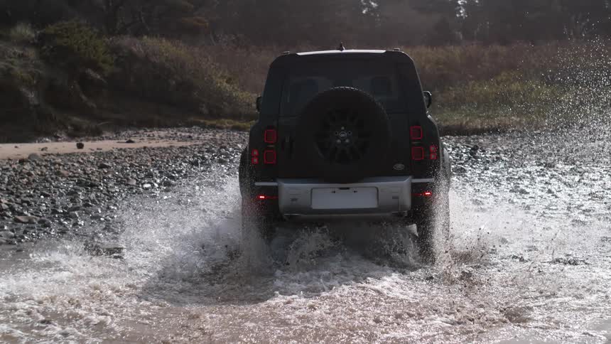 A sport utility vehicle drives along rocks on the coast