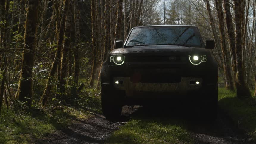 Land rover defender drives along dirt road in the forest