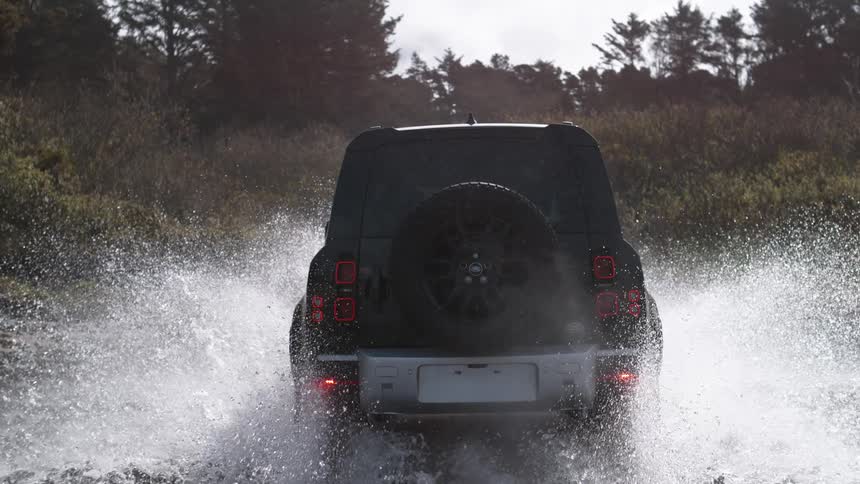 An all terrain car drives through a shallow body of water splashing it all around