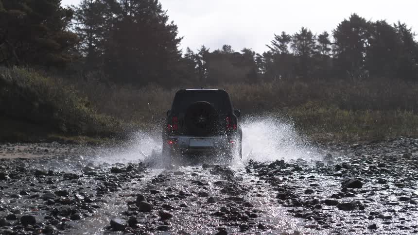 An suv drives through a muddy stream and splashes water around