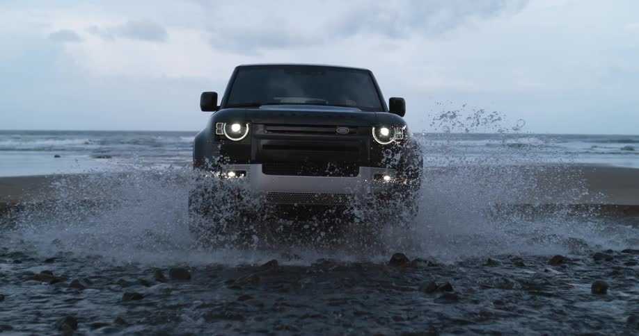 Vehicle splashes while driving through inlet on beach under cloudy sky