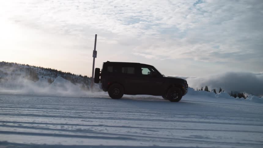 Black land rover defender drives down snowy road